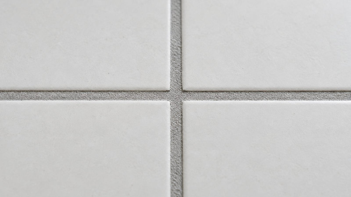 Close-up of light grey grout lines between white floor tiles