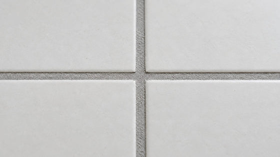Close-up of light grey grout lines between white floor tiles