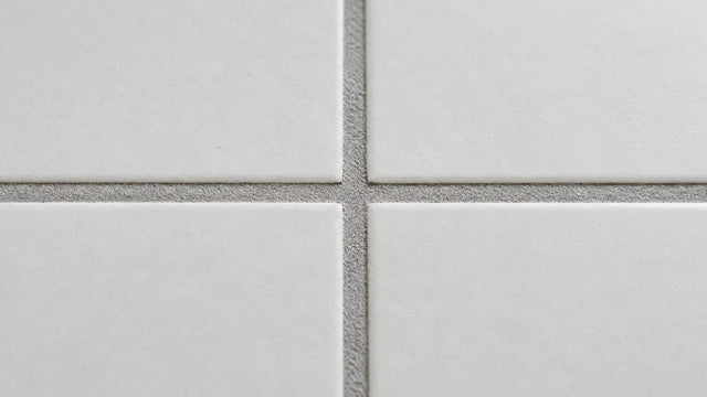 Close-up of light grey grout lines between white floor tiles